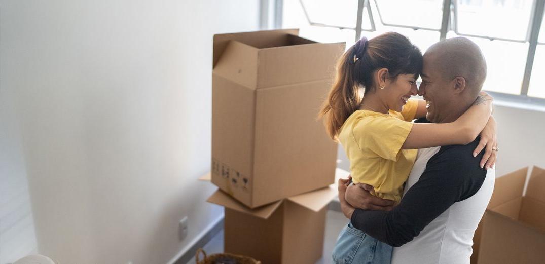 A couple hugs in front of moving boxes in their new home.